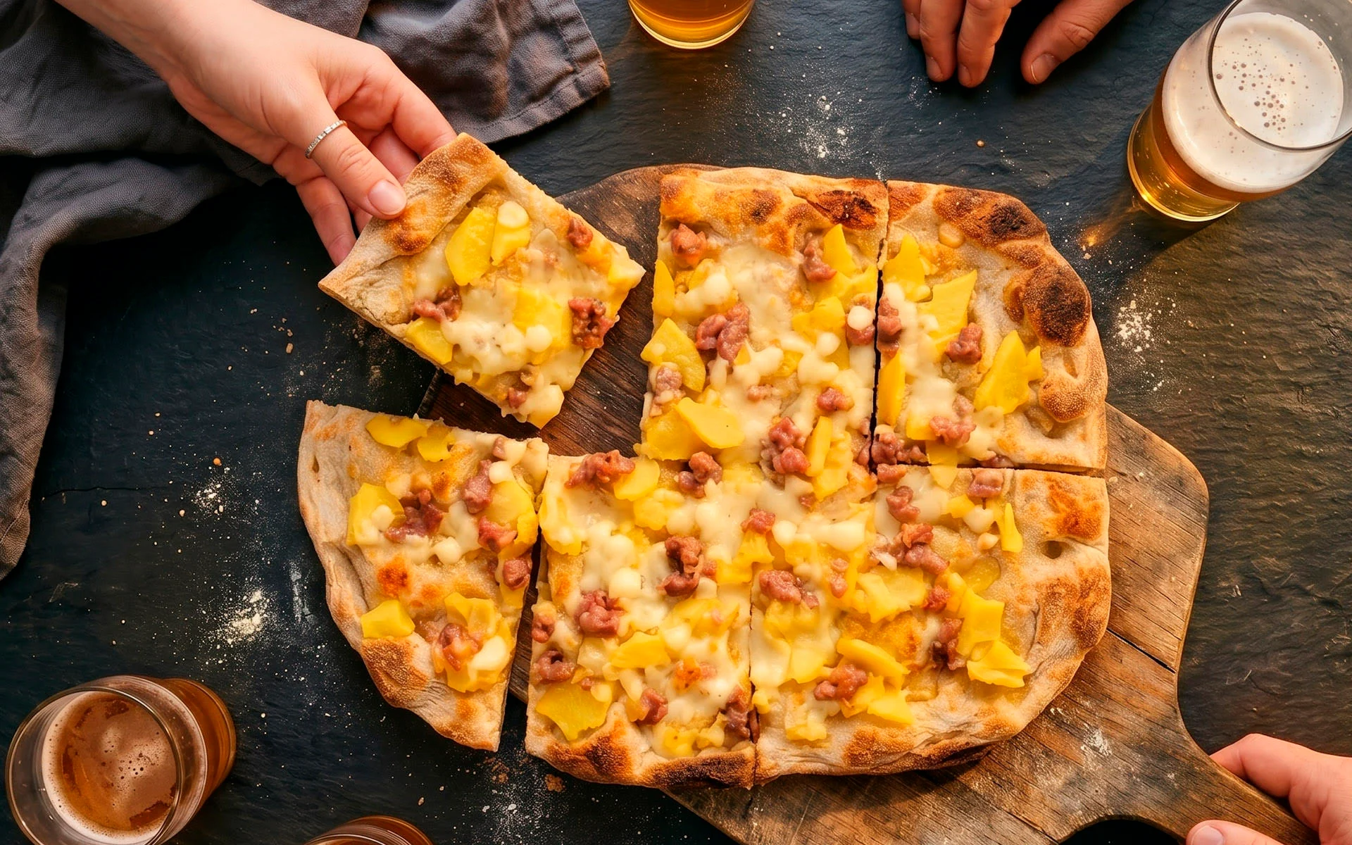 Een pinsa met aardappel en worst wordt aan tafel gedeeld
